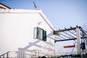 Un edifici blanc amb un balcó, una finestra amb persianes verdes i una barana de metall.