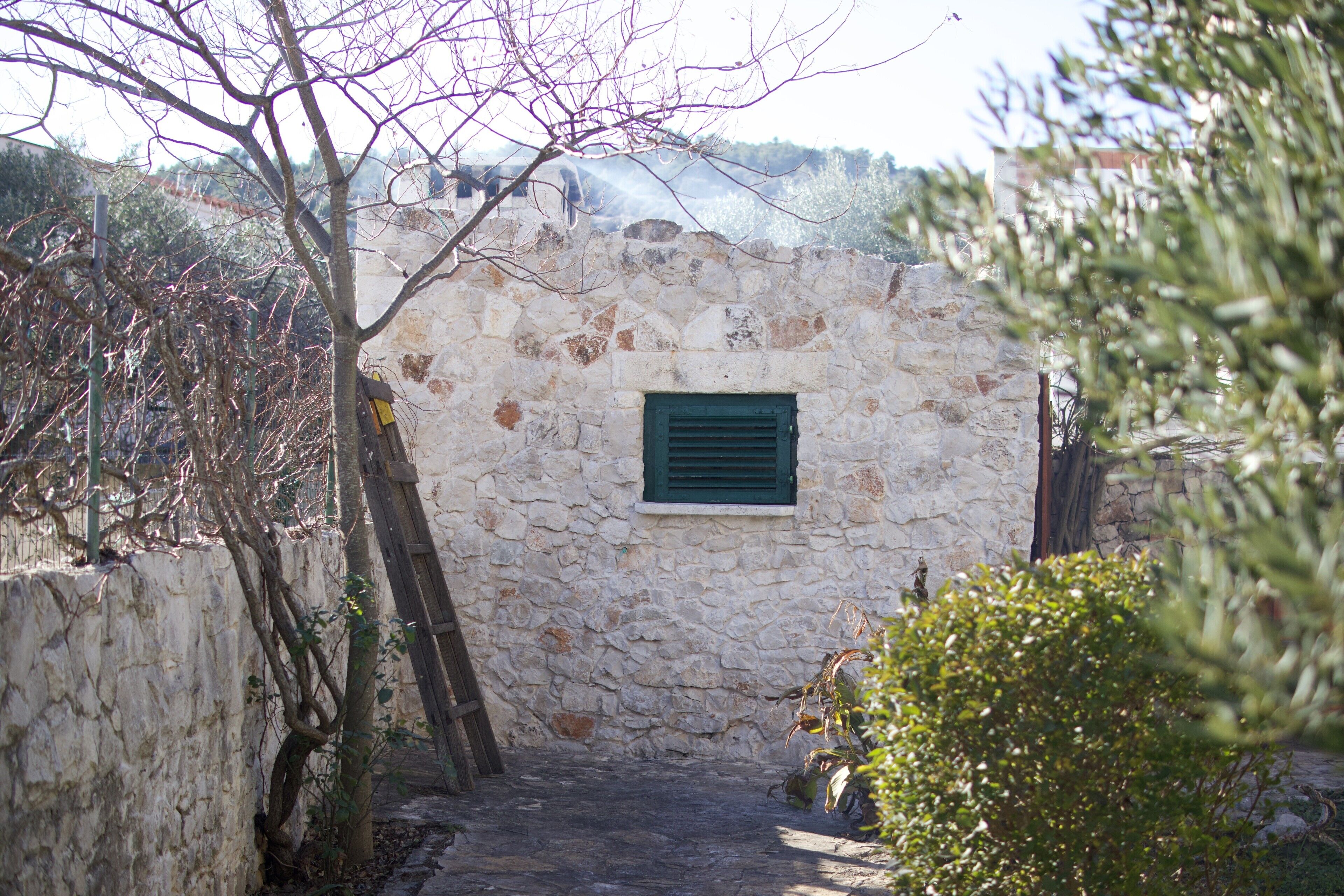 A narrow stone pathway leading to a rustic stone building with a green window.