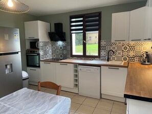 Una cocina moderna con armarios blancos, un refrigerador de acero inoxidable, microondas, lavavajillas y una ventana con persianas.