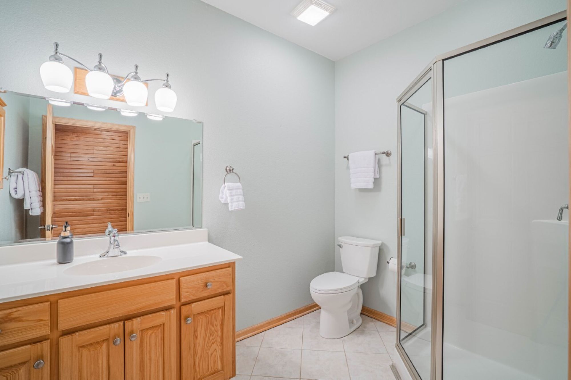 Een badkamer met een houten wastafelmeubel, een wit toilet en een douche met glazen wanden.