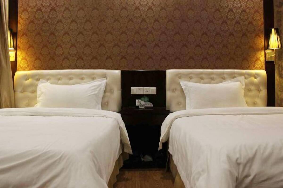 A hotel room with two beds, a nightstand, and a patterned wallpaper.