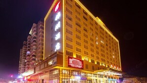 A multi-story hotel with a prominent red logo on the facade, large illuminated windows, and a ground-level entrance with visible signage. - Kumho Hotel (Wengyuan)