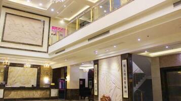 A hotel lobby with a reception desk, a large artwork, a chandelier, and a staircase.