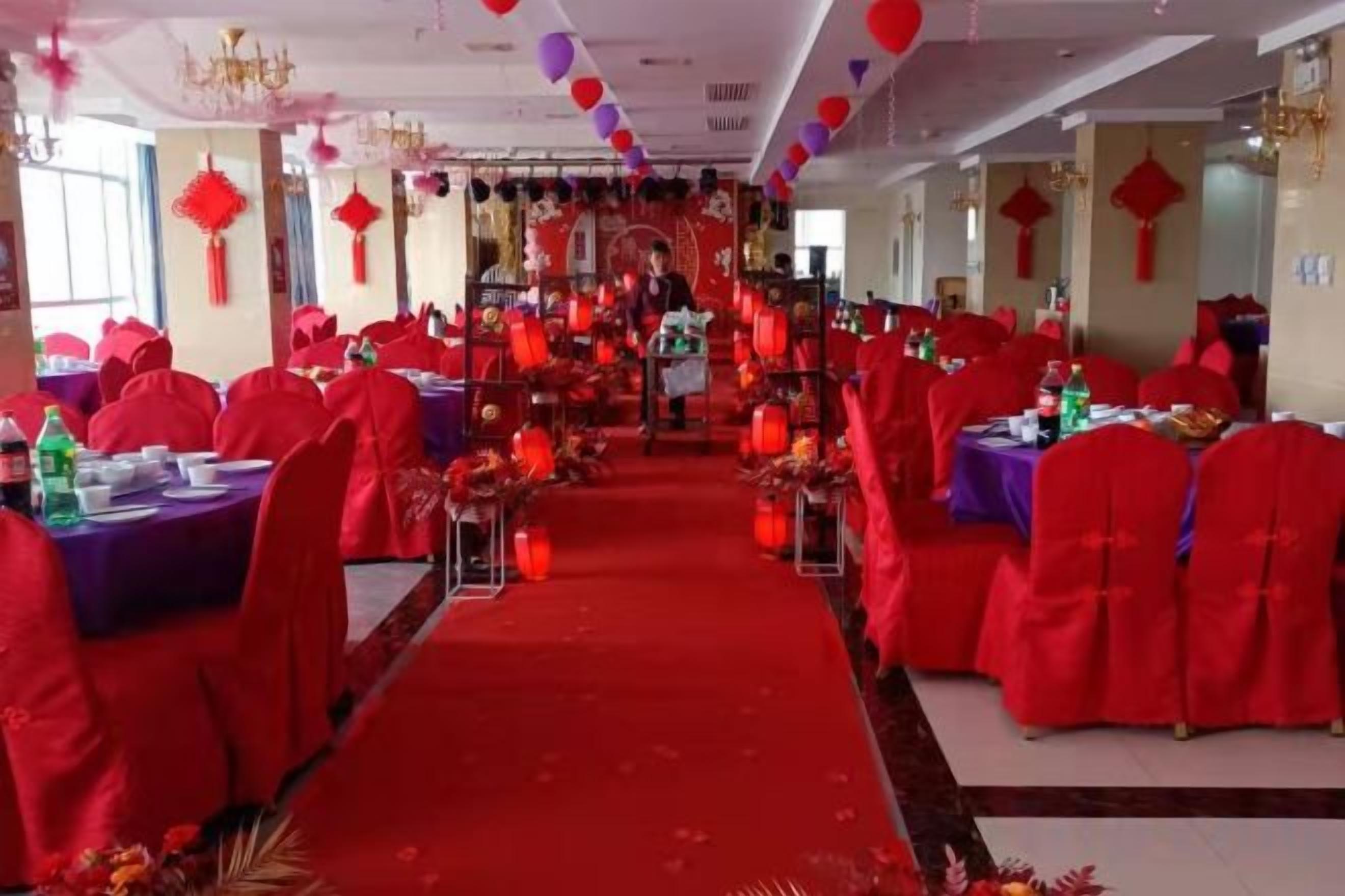 A banquet hall with tables arranged in rows, red chairs, and a central aisle.