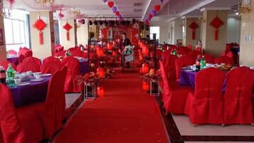 A banquet hall with tables arranged in rows, red chairs, and a central aisle.