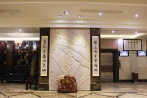 A lobby with a reception desk, a large decorative wall, and an elevator. - Kumho Hotel (Wengyuan)