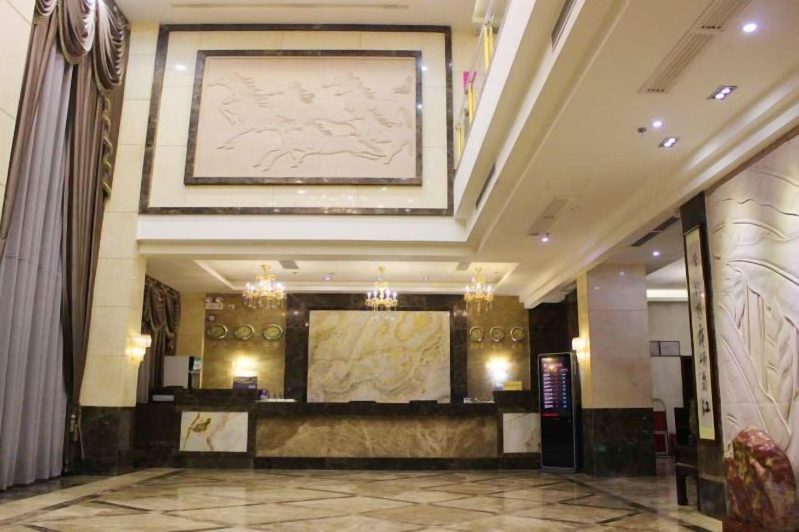Rebedor d'hotel amb una taquilla d'adreça, lluminàries penjants, un mural gran i un paviment de marbre.