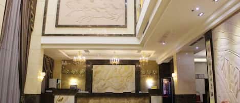 A hotel lobby with a reception desk, chandeliers, a large mural, and a marble floor.