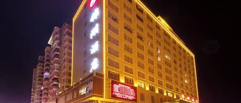 Un hotel de varios pisos con señalización iluminada y un logotipo rojo destacado en la fachada.