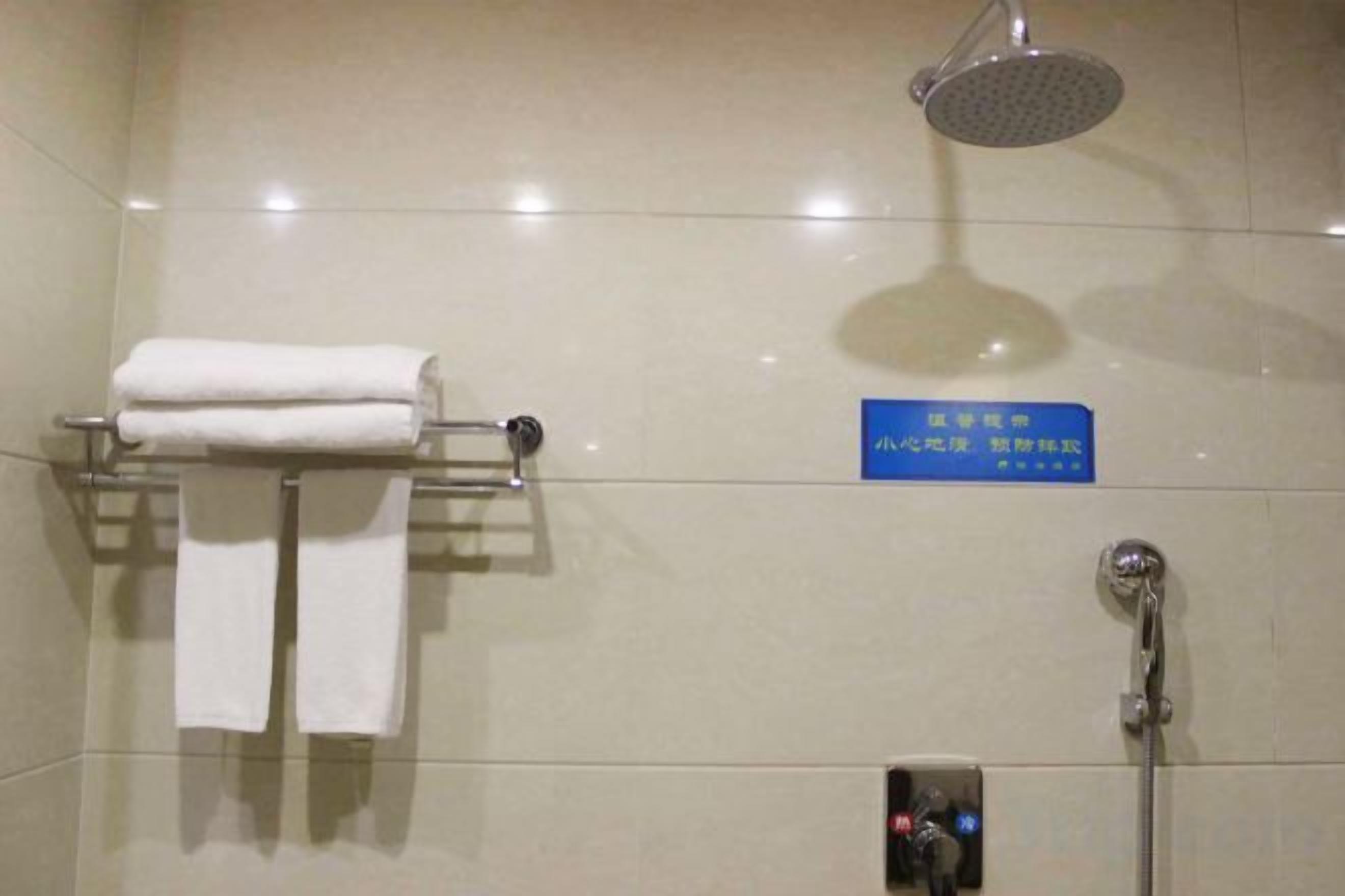 A bathroom with a shower, a towel rack with towels, and a sign with text.