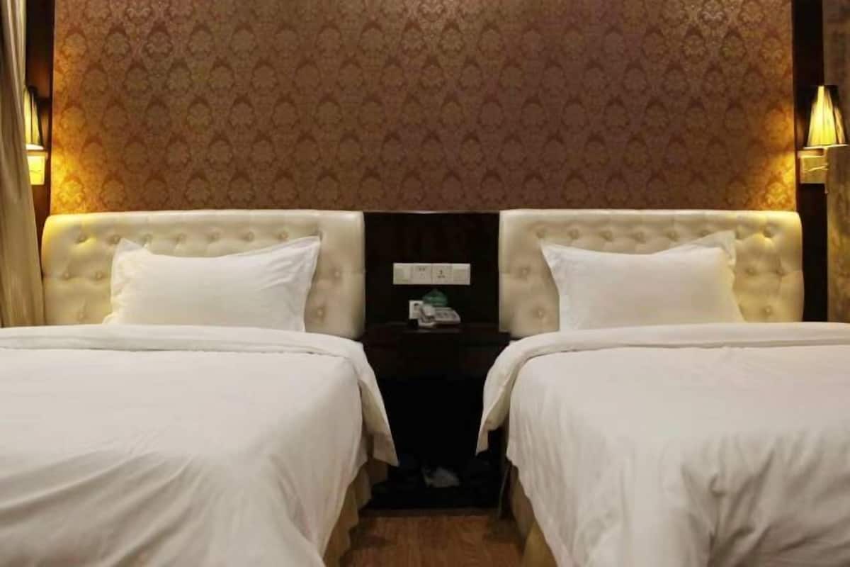 A hotel room with two beds, a nightstand, and a wall with a patterned wallpaper.
