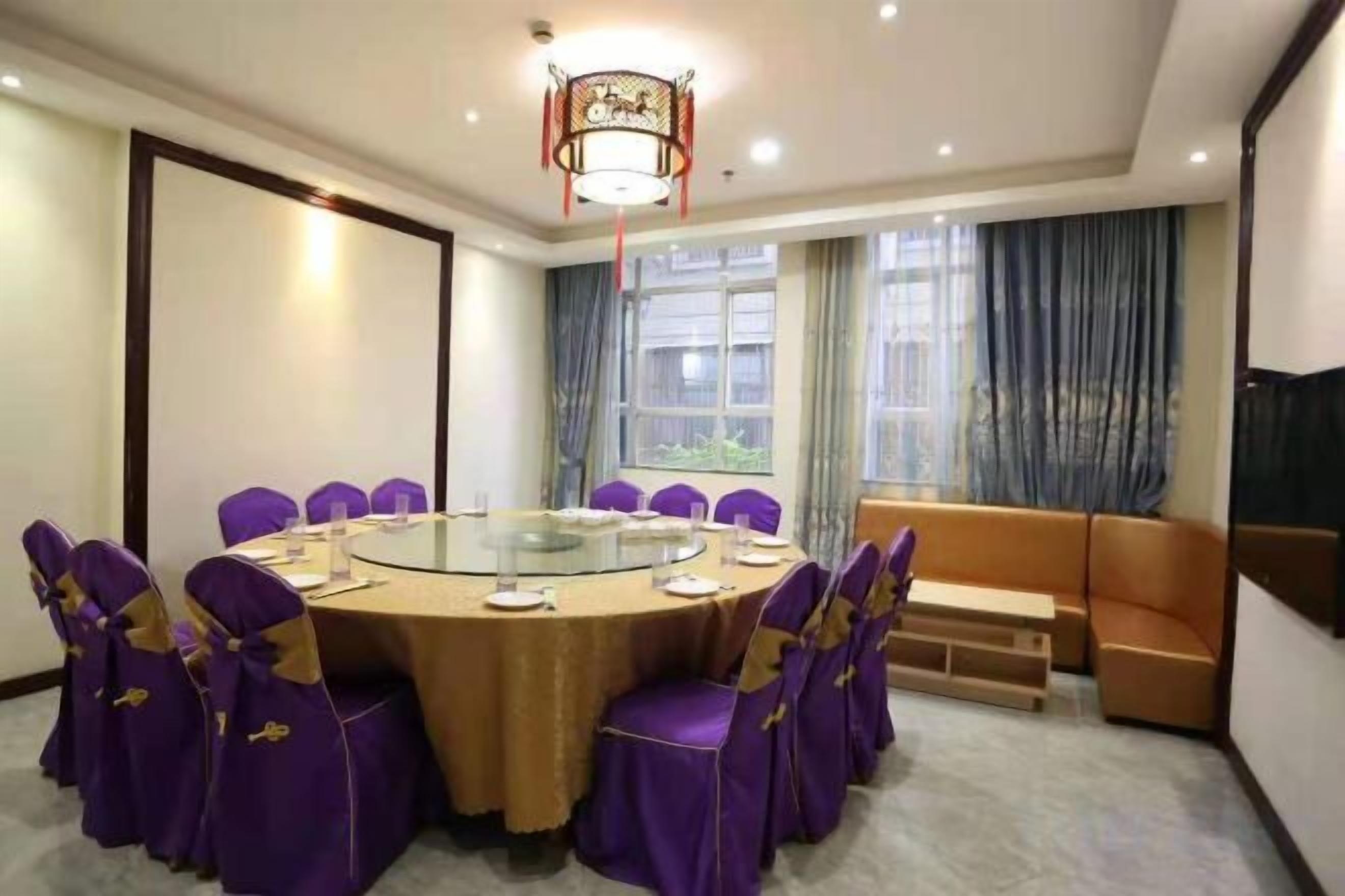 A conference room with a round table, purple chairs, a sofa, and a large window with curtains.