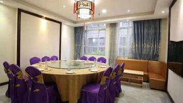 A conference room with a round table, purple chairs, a sofa, and a large window with curtains.