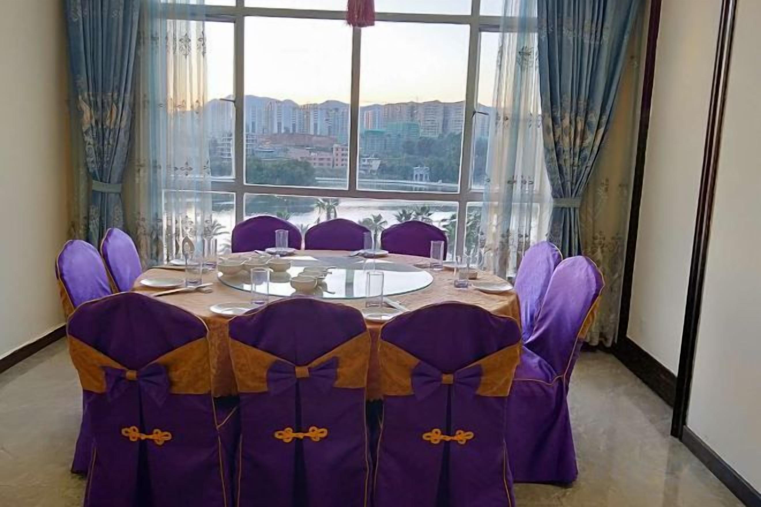 A dining area with a round table, purple chairs, and a view of buildings through large windows.