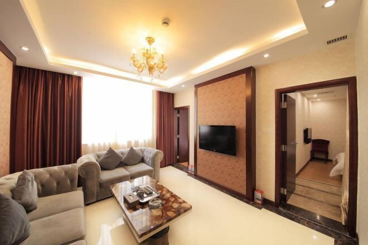 A modern living room with a sofa set, a coffee table, a flat-screen TV, and a chandelier.