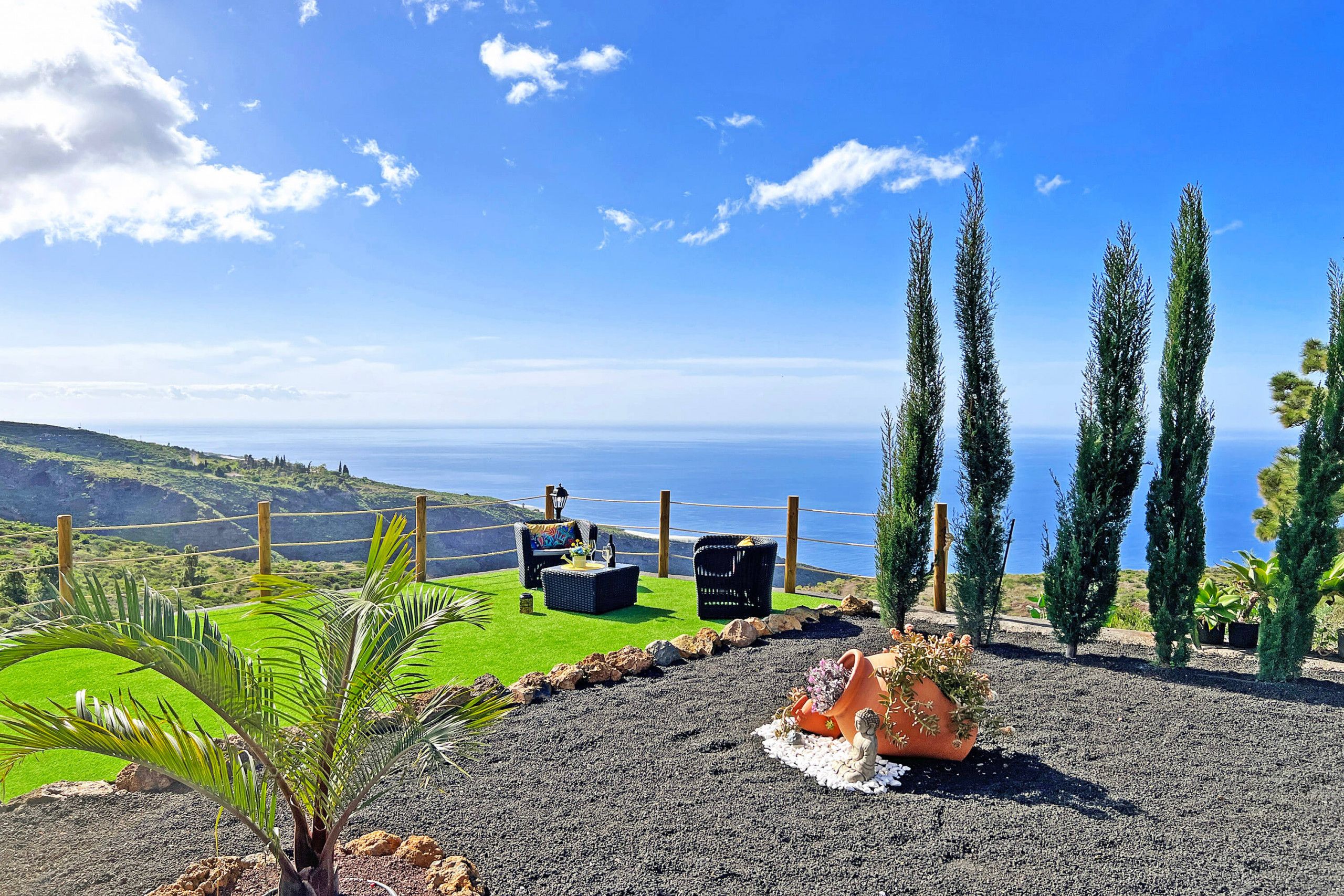A terrace with seating, a view of the sea, and a landscaped area with plants.