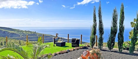 A terrace with seating, a view of the sea, and a landscaped area with plants.