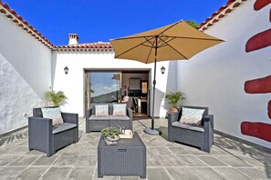 An outdoor patio with wicker furniture, a large umbrella, and potted plants. - Casas García, Tijarafe (Tijarafe)