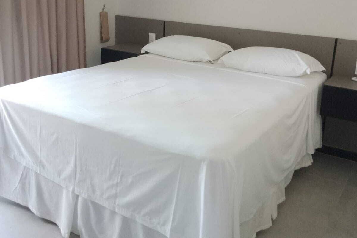 A neatly made bed with white bedding, a headboard, and a nightstand with a lamp.