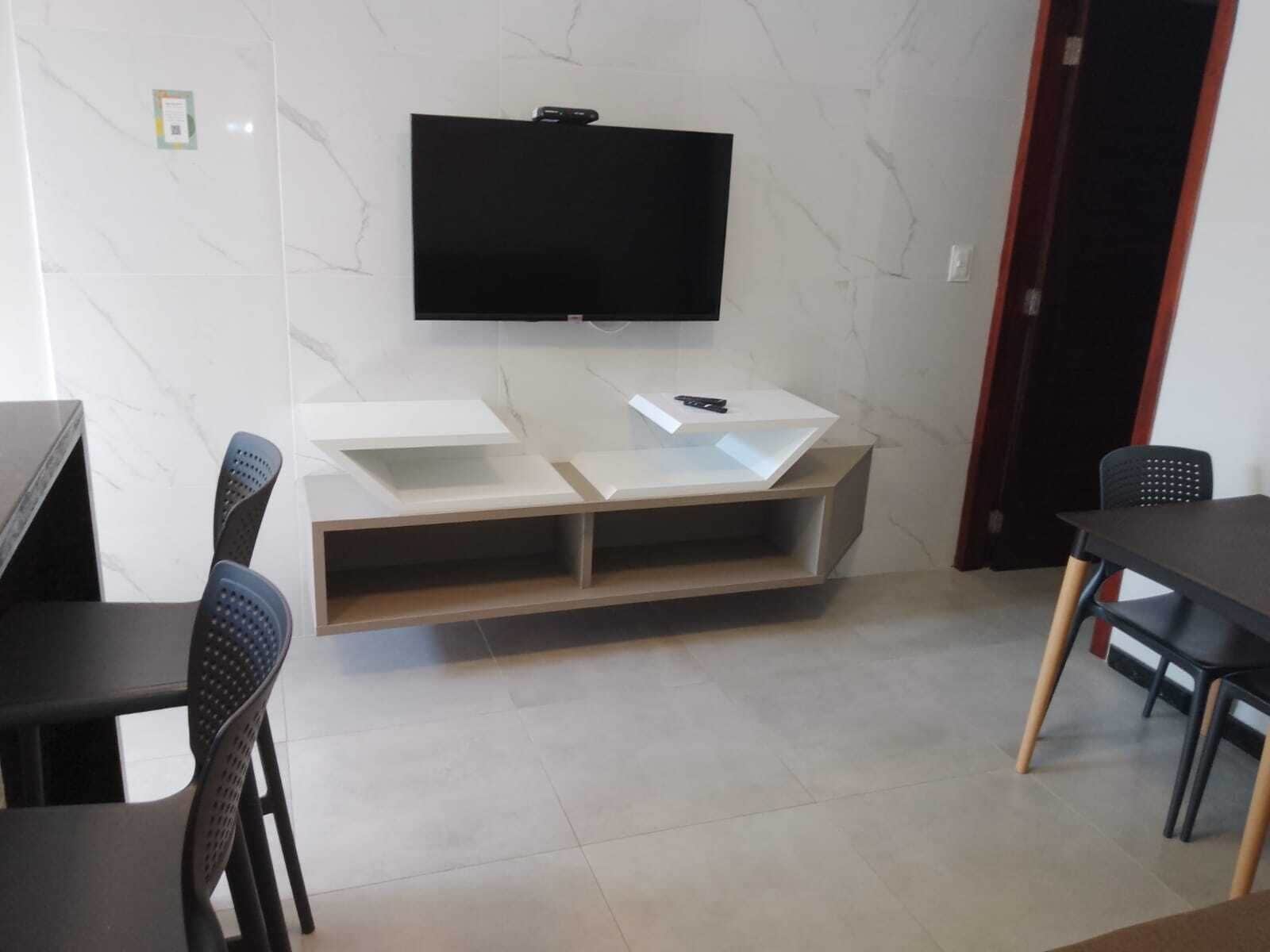 A modern living room with a flat-screen TV mounted on the wall, a white console table with a remote, and two black chairs.