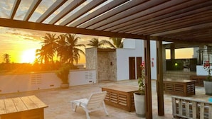 An outdoor patio area with a pergola, seating, and a view of palm trees at sunset. - Terraço Flecheiras (Trairi)