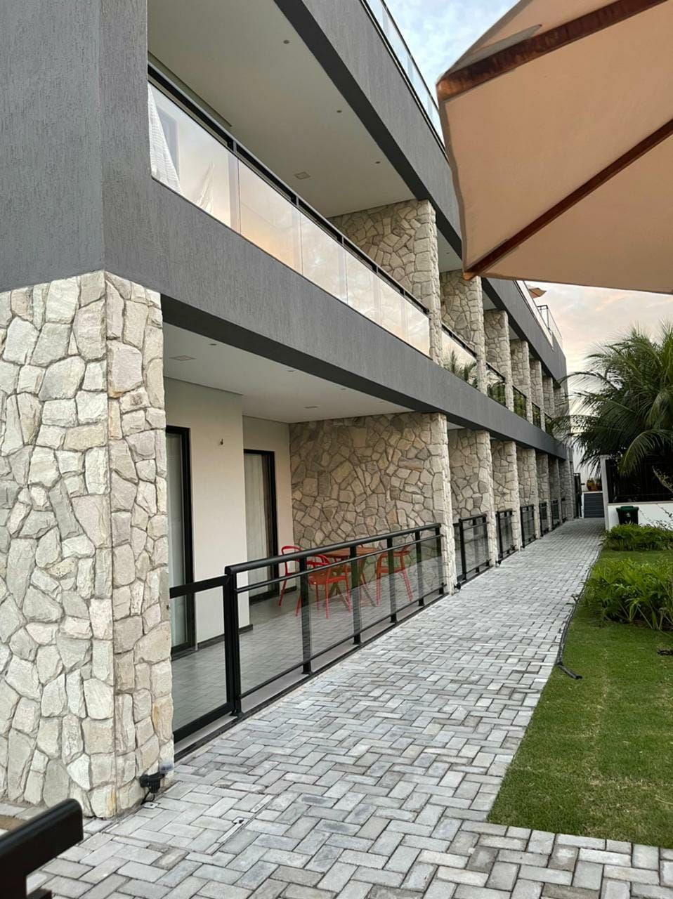 Un edificio moderno con fachada de piedra, un área de estar al aire libre techada y un camino pavimentado.