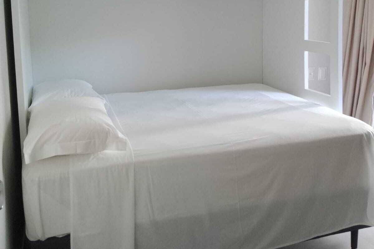 A bunk bed with a white mattress and bedding, a small window on the upper bunk, and a curtain on the right side.