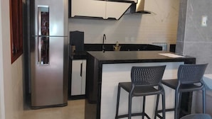 A modern kitchen with a stainless steel refrigerator, black cabinets, a black countertop, and two black bar stools. - Terraço Flecheiras (Trairi)
