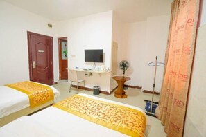 A hotel room with two beds, a desk, a chair, a television, a fan, and a curtain.