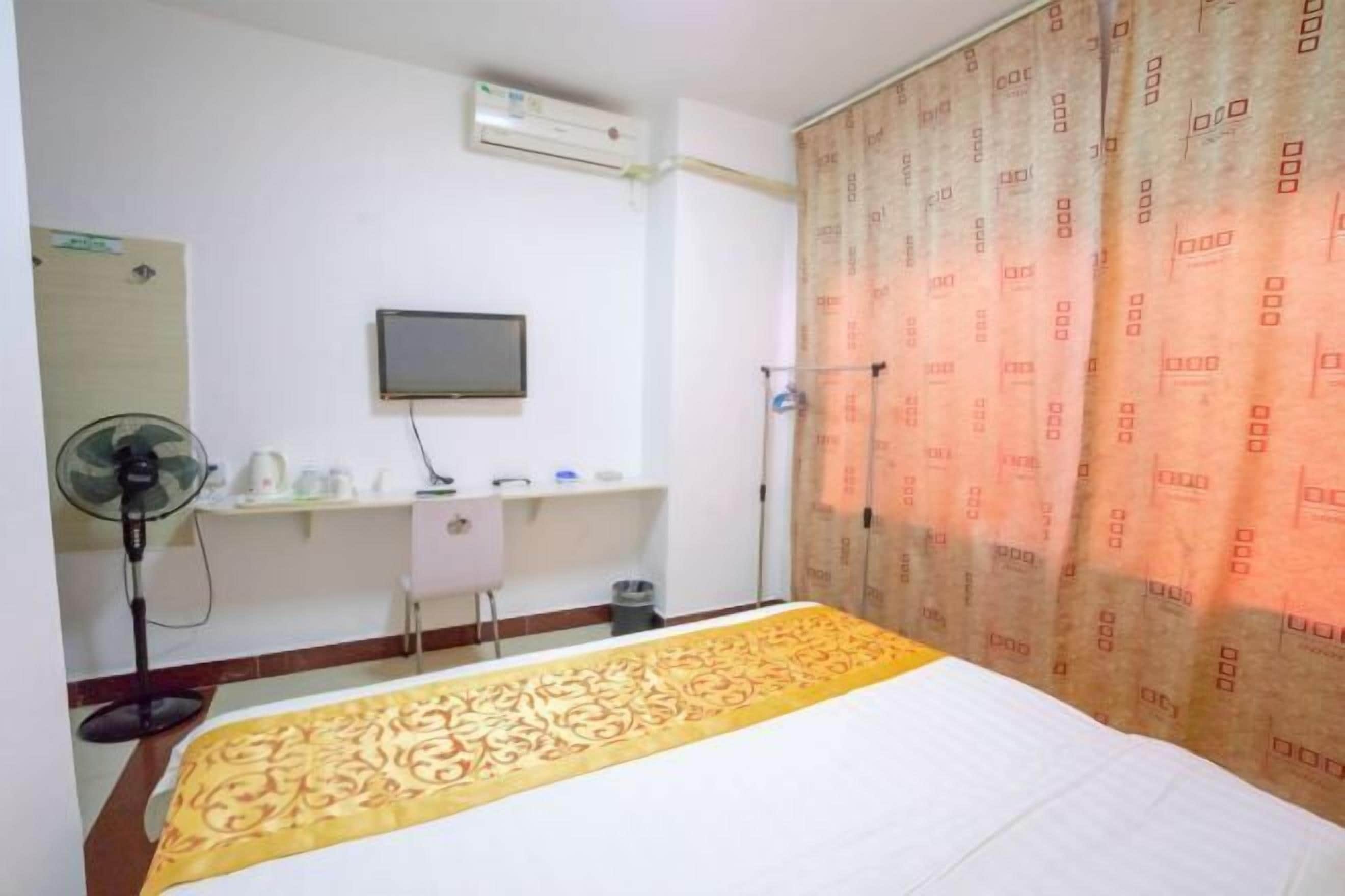A hotel room with a bed, a desk, a chair, a TV, and a window with curtains.