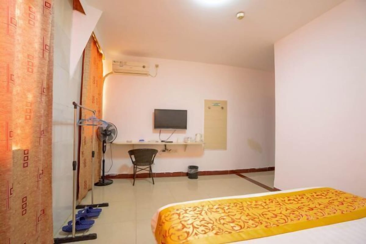 A hotel room with a bed, a desk, a chair, a television, and a window.