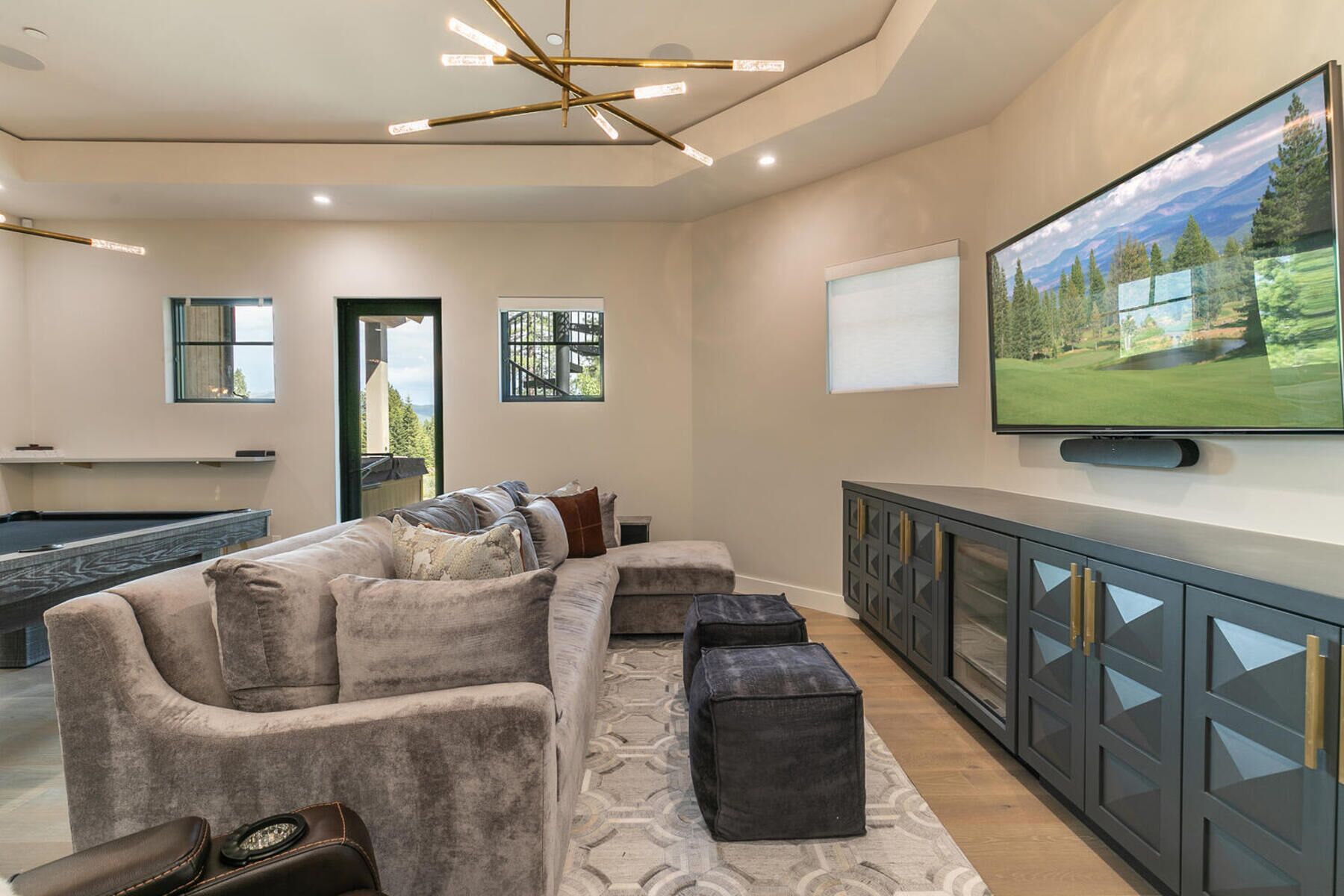 Una sala de estar moderna con un sofá modular, otomanas, una mesa de billar, un televisor montado en la pared y vistas a un paisaje montañoso.