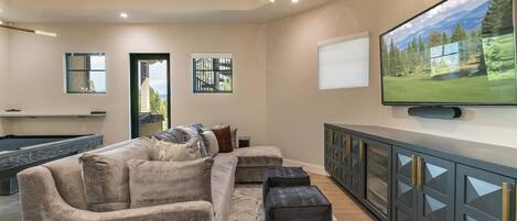 Una sala de estar moderna con un sofá modular, otomanas, una mesa de billar, un televisor montado en la pared y vistas a un paisaje montañoso.
