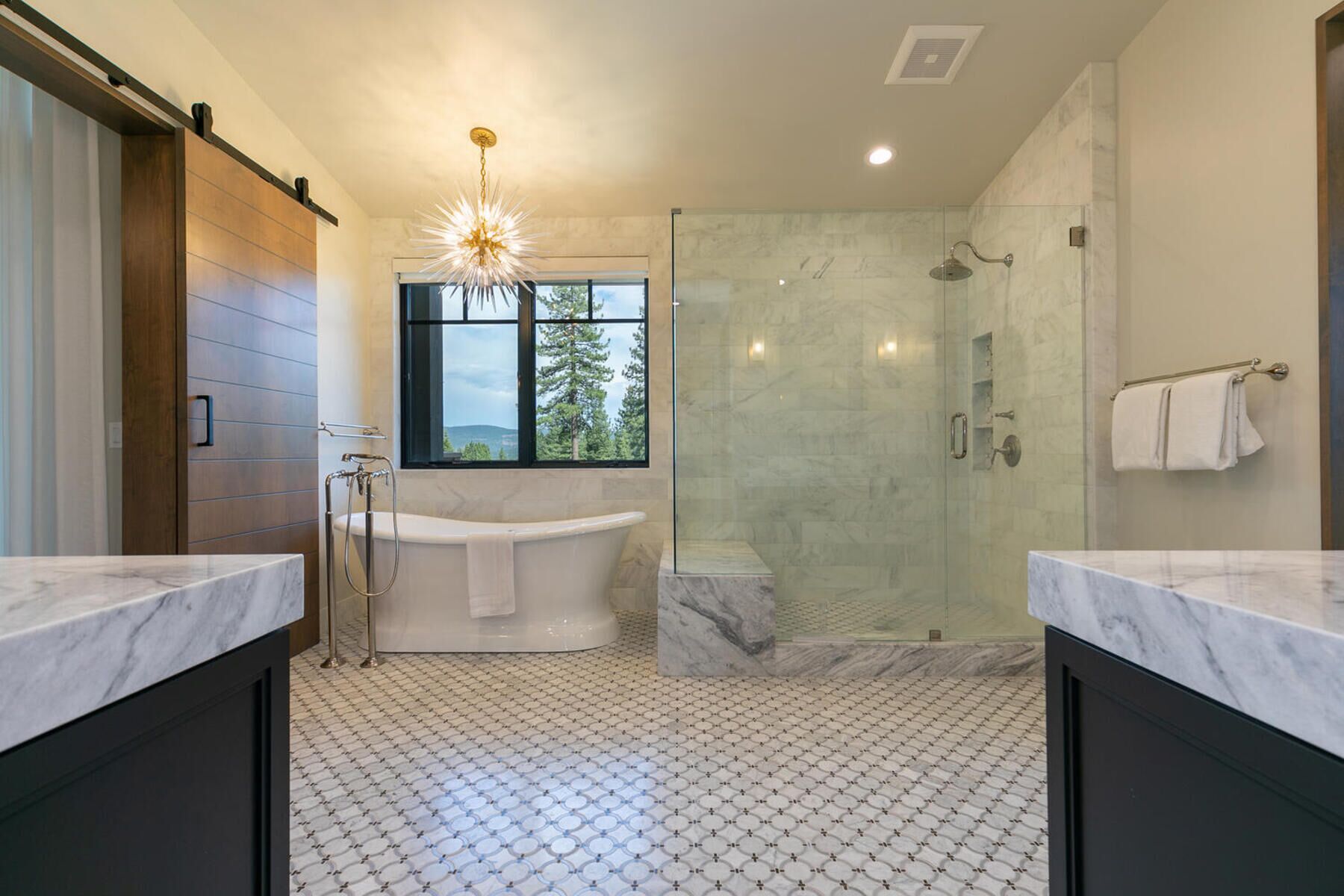 Ein modernes Badezimmer mit einer freistehenden Badewanne, einer Duschkabine und einem großen Fenster mit Blick auf Bäume.