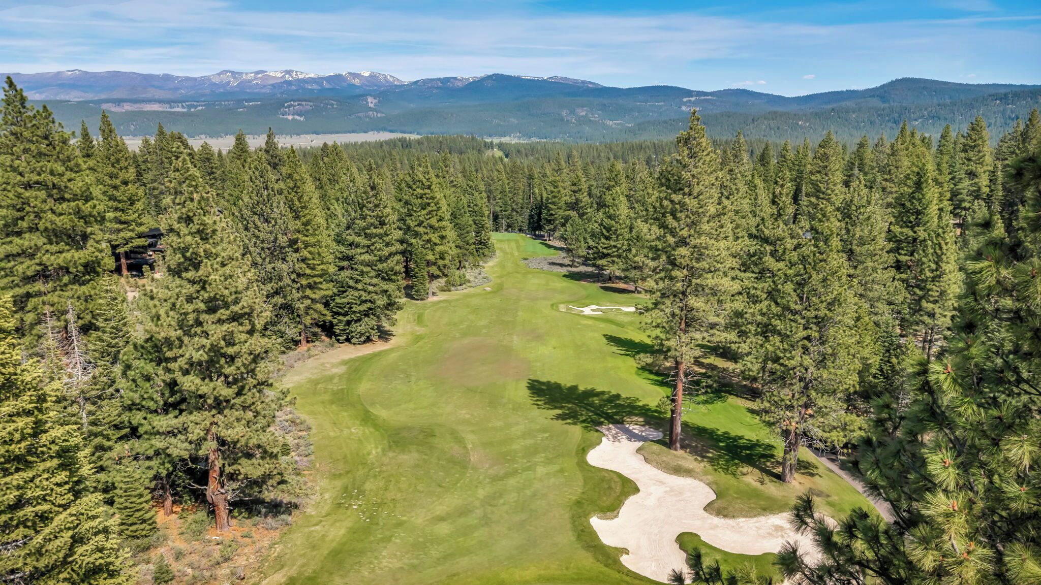 Un parcours de golf entouré d’une forêt dense, avec des montagnes en arrière-plan.