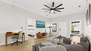 A spacious living room with a wooden floor, a ceiling fan, a desk with a chair, a sofa set, and a painting on the wall. - Spacious 4BR Beach House w/ Pool | Pura Vida (North Myrtle Beach)