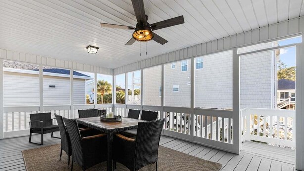 A covered outdoor patio with a table and chairs, a ceiling fan, and large windows. - Spacious 4BR Beach House w/ Pool | Pura Vida (North Myrtle Beach)