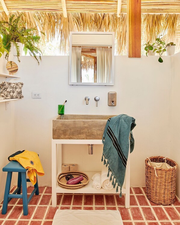 A bathroom with a wooden vanity, a mirror, a towel rack, a green plant, and a blue stool.