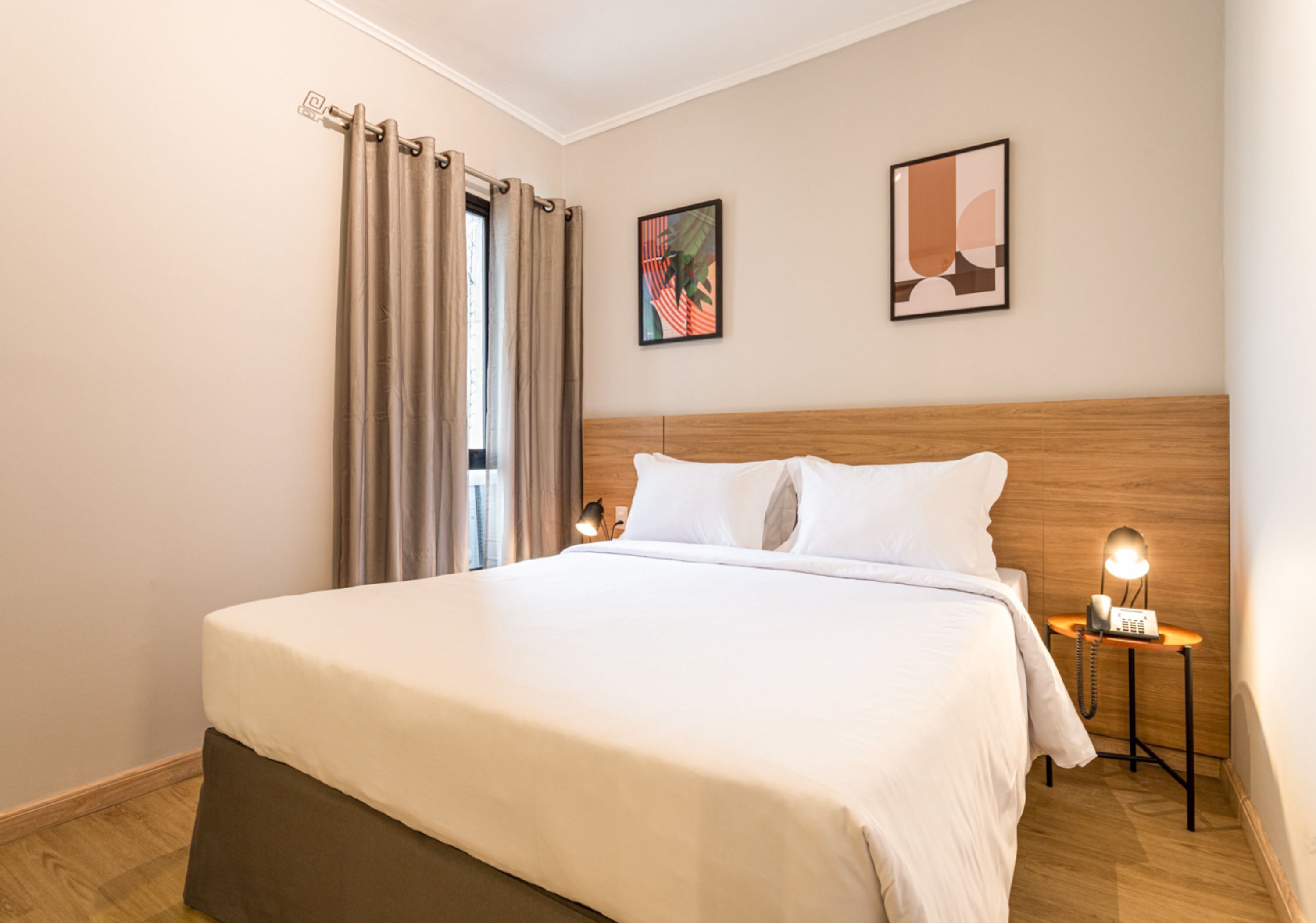 A neatly made bed with white linens, a wooden headboard, and a bedside table with a lamp and a telephone.