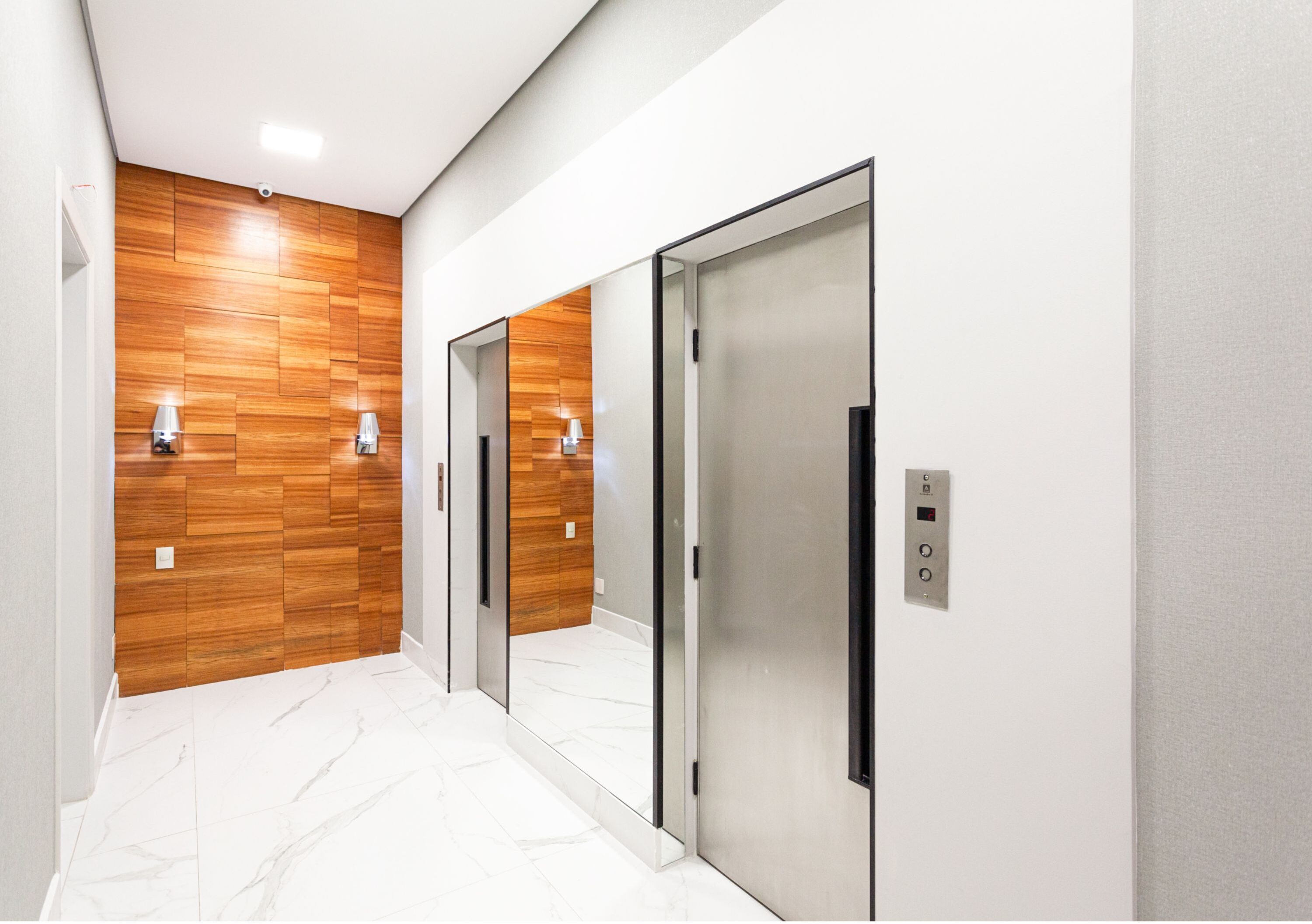 A modern elevator with a metallic finish, a wooden panel wall, and a white marble floor.