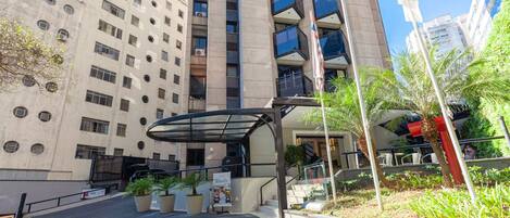A multi-story building with a covered entrance, potted plants, and a flag.