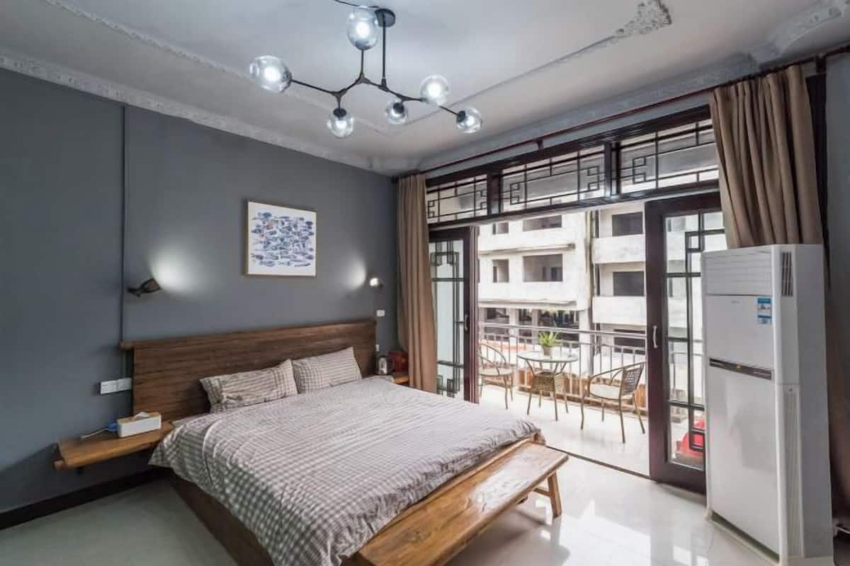 A bedroom with a bed, bedside table, and a view of an outdoor balcony.