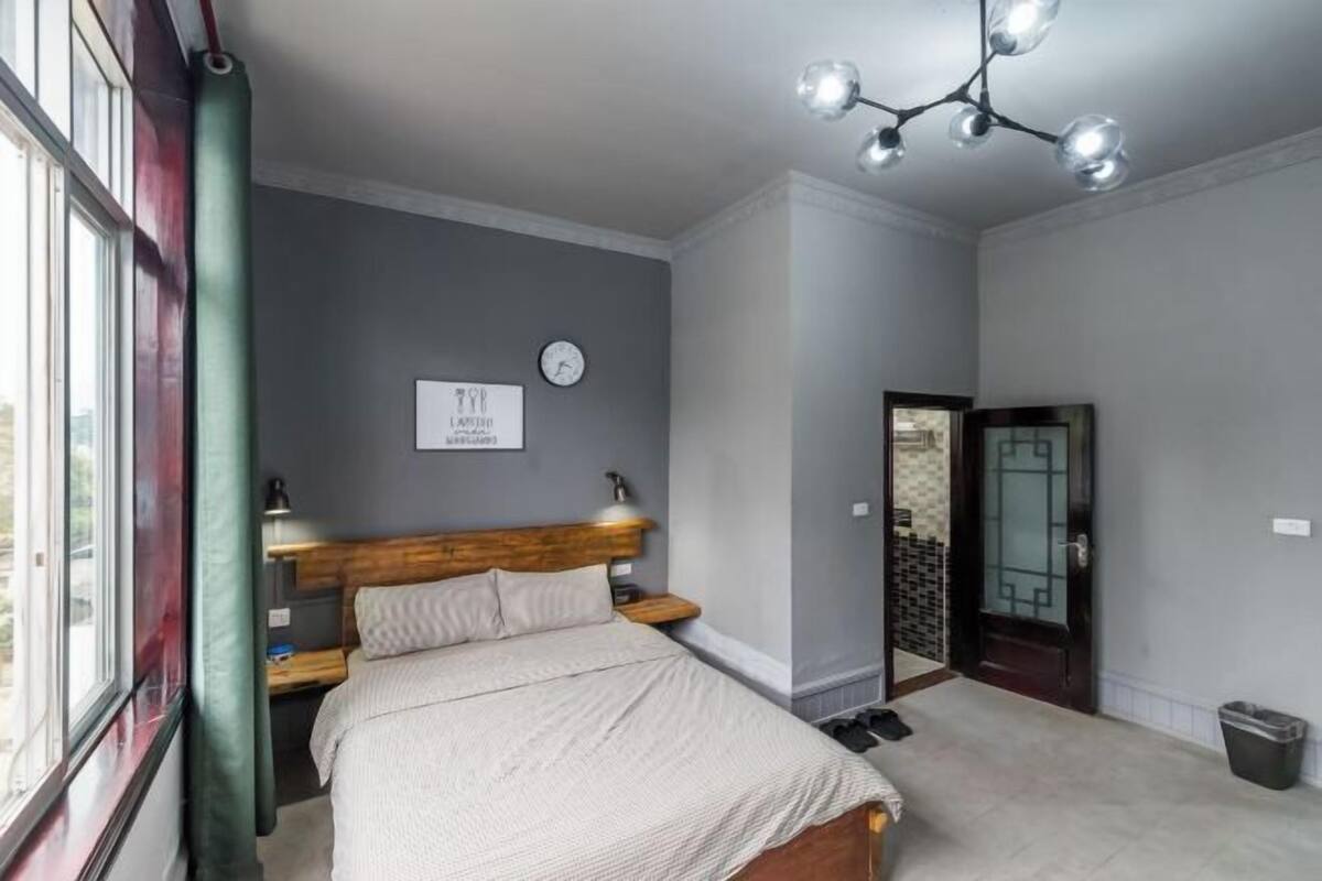 A bedroom with a bed, bedside table, lamp, clock, and a door leading to another room.