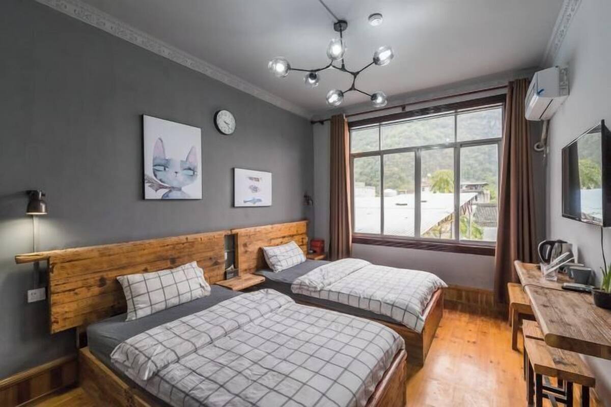A bedroom with two beds, a wooden headboard, a desk, a chair, a window with curtains, and wall art.