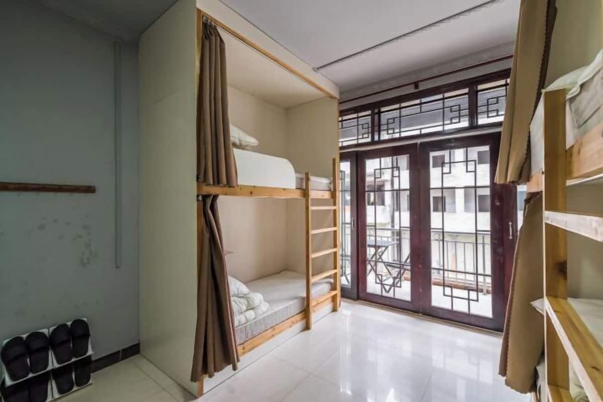 A dormitory room with bunk beds, a shoe rack, and a view through a large window.