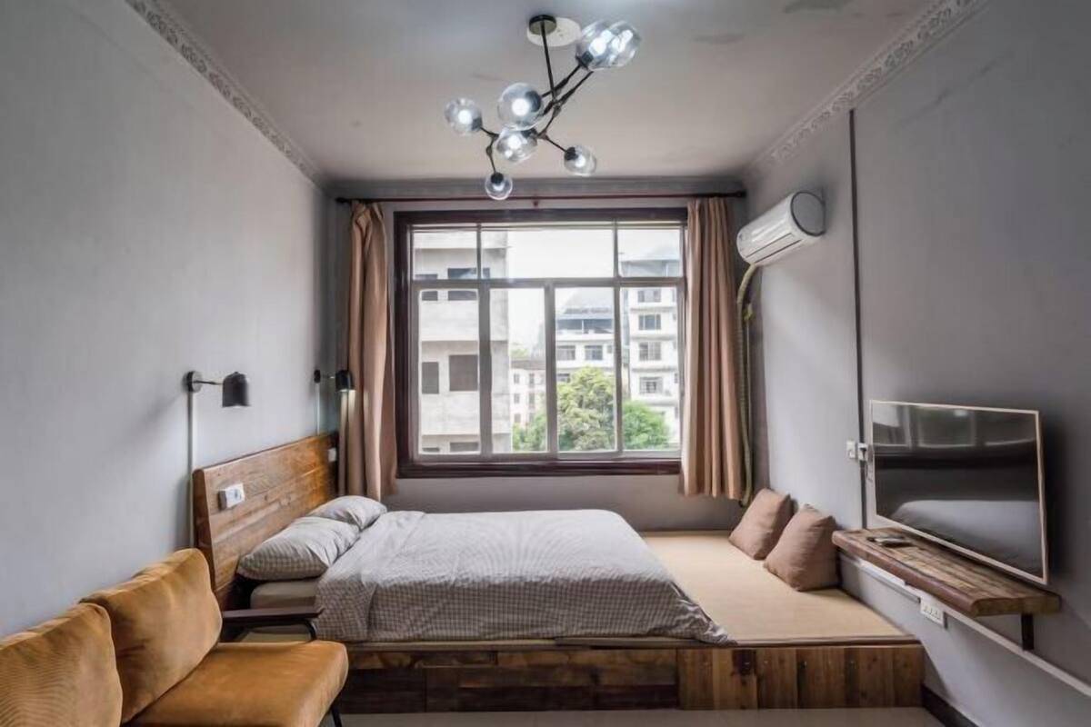A bedroom with a bed, a TV, a window, and a ceiling light fixture.