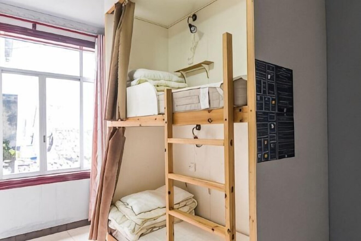 A bunk bed with storage shelves, a window with curtains, and a wall-mounted electrical panel.
