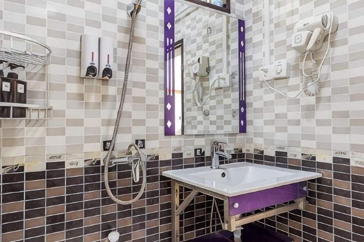 A bathroom with a checkered tile wall, a white sink, a mirror with a purple frame, a towel rack, and a shower area.