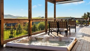 Una terraza de madera con un jacuzzi, sillas y vistas a un paisaje verde.