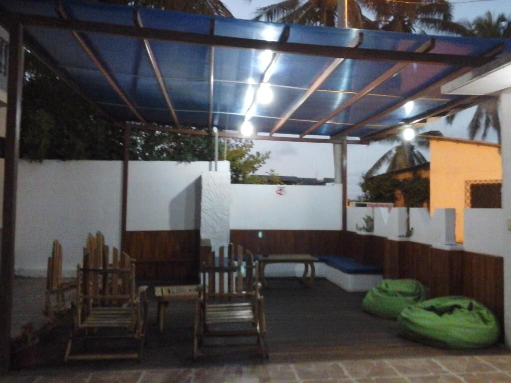 Un patio al aire libre con zona de estar techada, una mesa y dos puffs verdes.